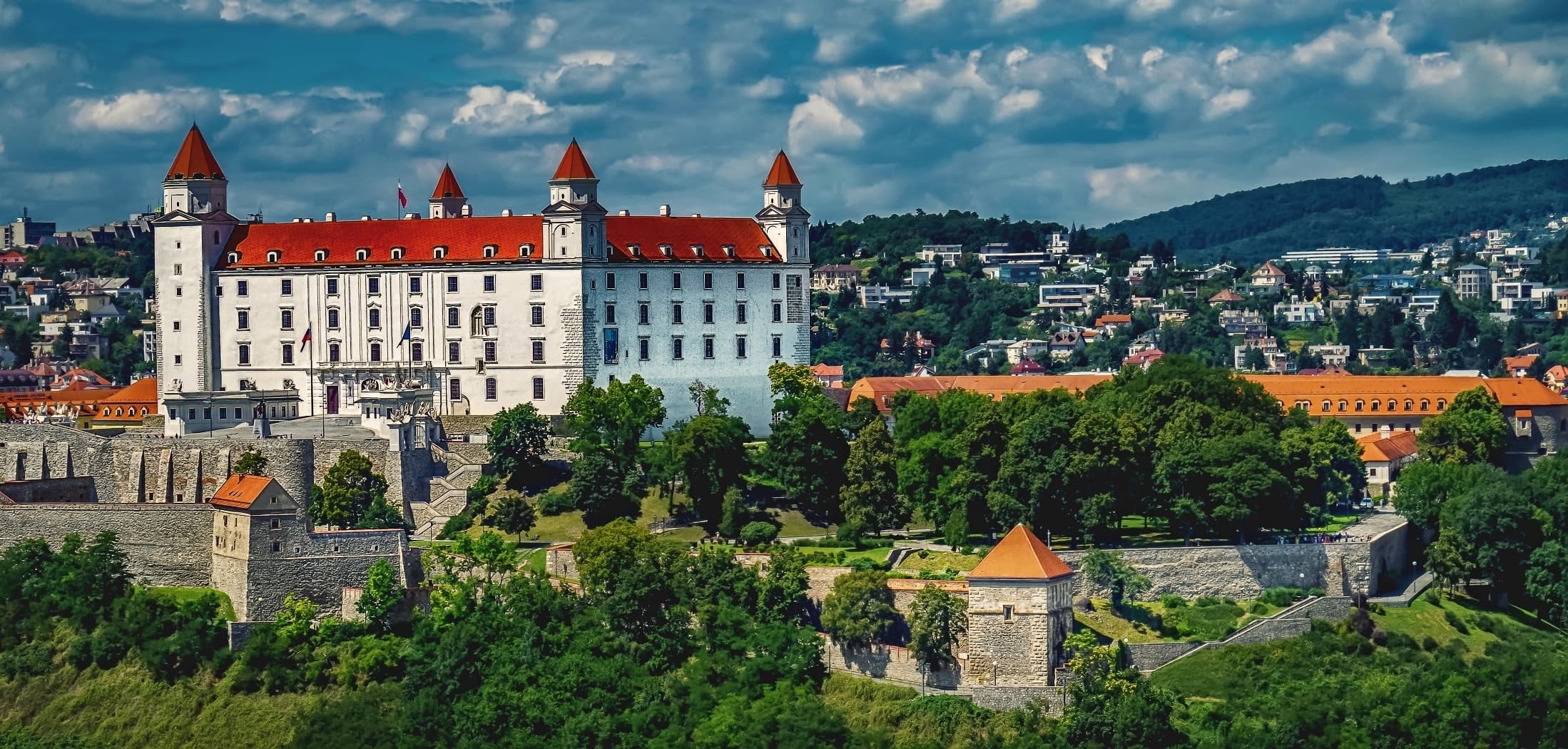 Bratislavský hrad s bielymi múrmi a červenými strechami veží nad mestom